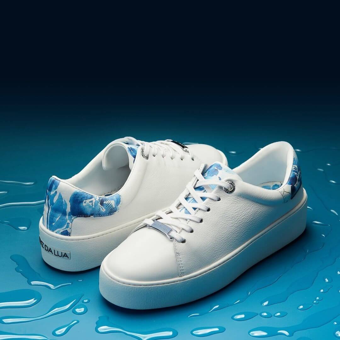 Tênis branco com destalhe em azul estilo clean com fundo azul água.
